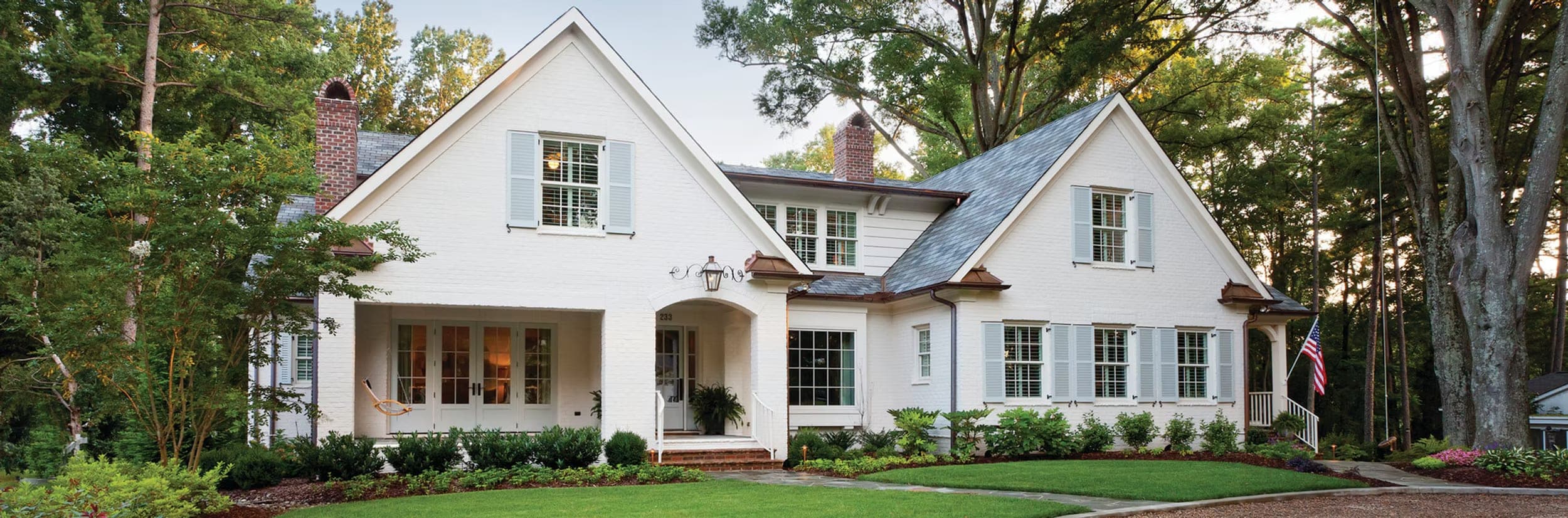 A white brick home with a manicured lawn and fresh landscaping