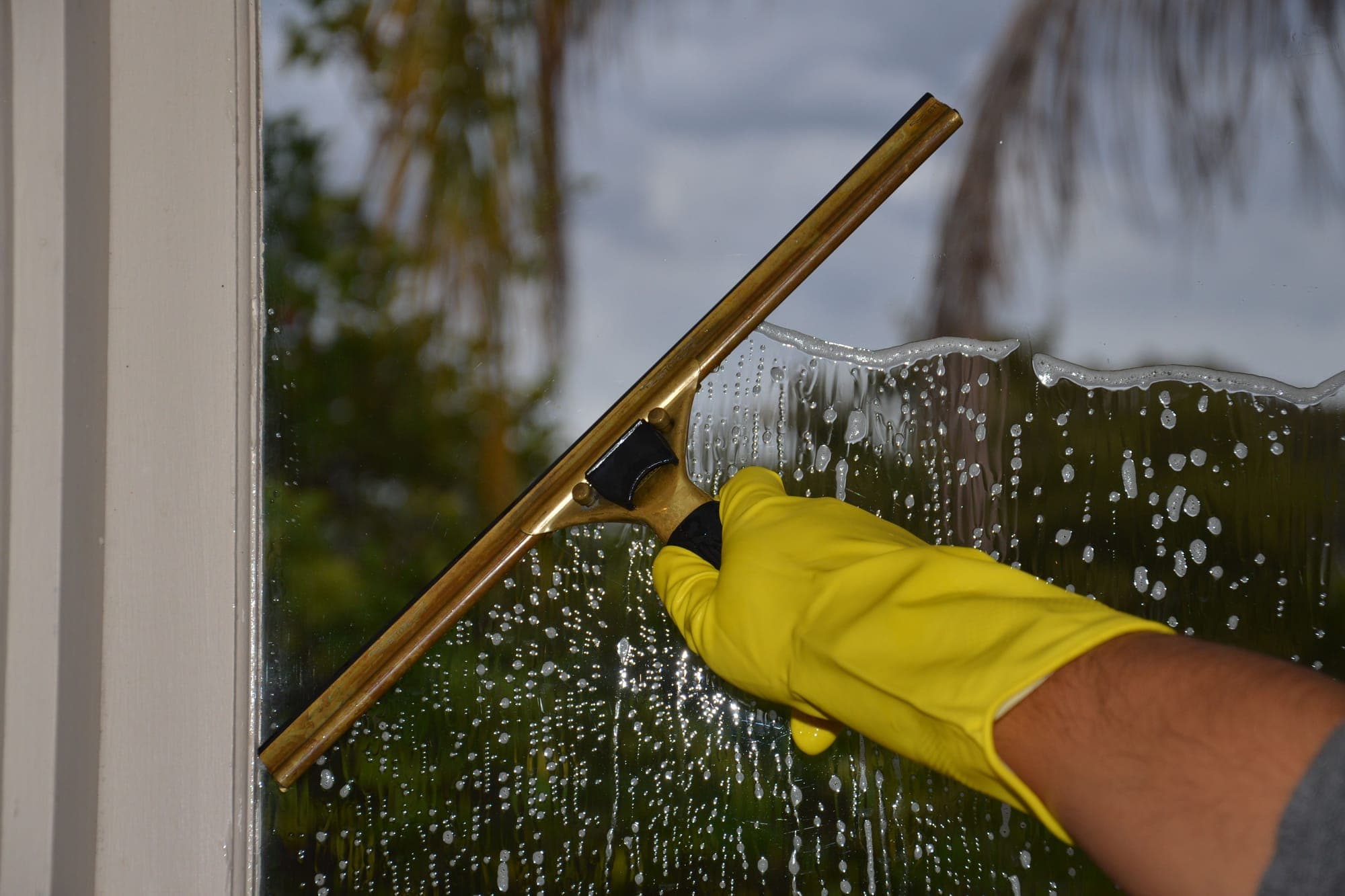 A gloved hand pulling a squeegee down a soapy window