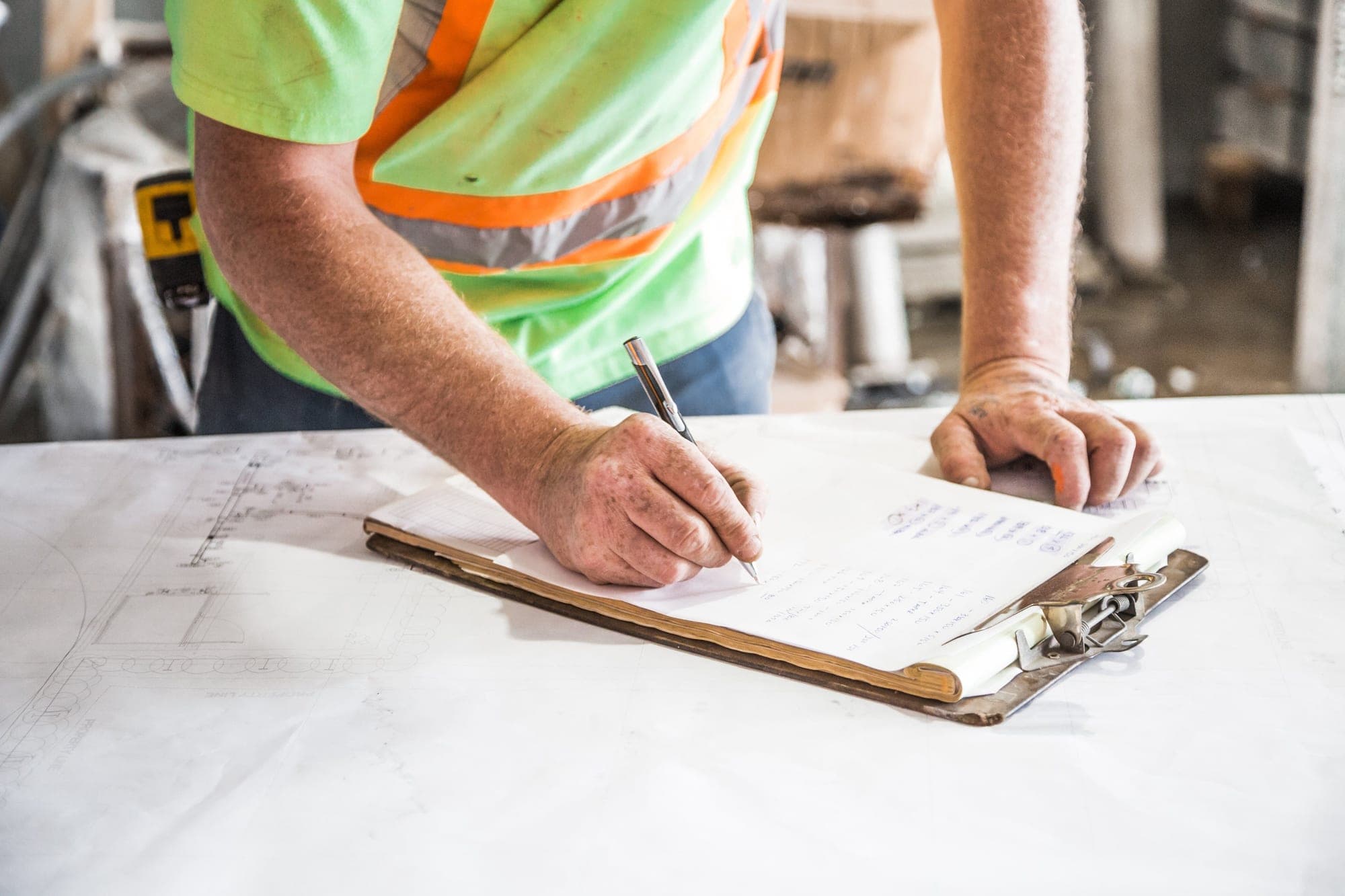A worker in a safety vest taking notes on a clipboard over a set of site plans